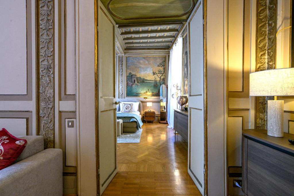 View through double doors into a bedroom with a mural of a seaside scene, wooden floor, bed with white and blue bedding, nightstand with lamp, and ornate wall paneling.