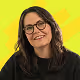 Smiling woman with long dark hair and glasses against a bright yellow background.