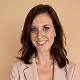 Smiling woman with wavy brown hair wearing a light pink blazer and white top.