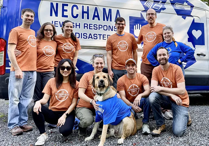 Group of volunteers wearing orange and blue FI Service Corps t-shirts posing with a dog in front of a NECHAMA Jewish Response to Disaster van.