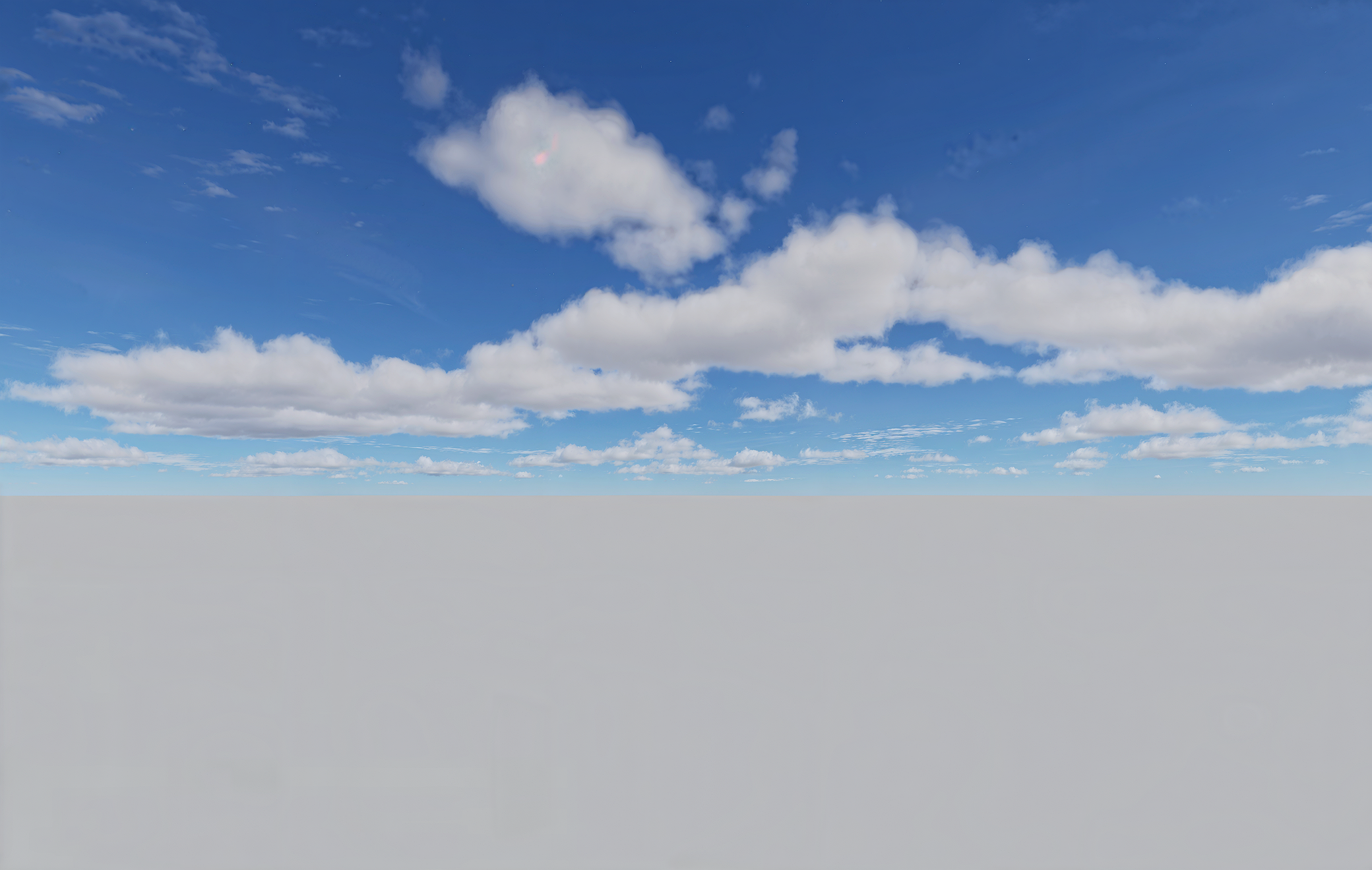 Niebieskie niebo z rozproszonymi białymi chmurami nad szarą, pustą powierzchnią.