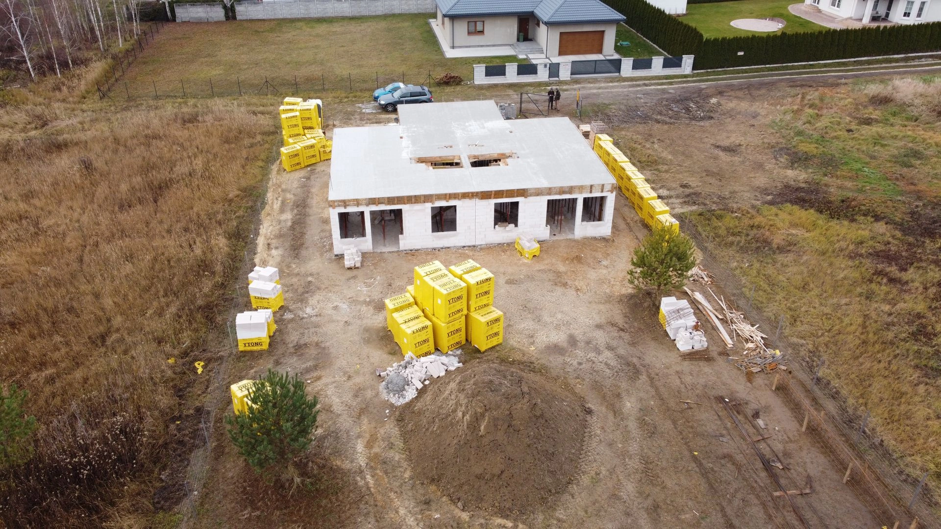 Budowa domu jednorodzinnego na etapie wznoszenia ścian i stropu, na placu rozłożone materiały budowlane i ziemia.