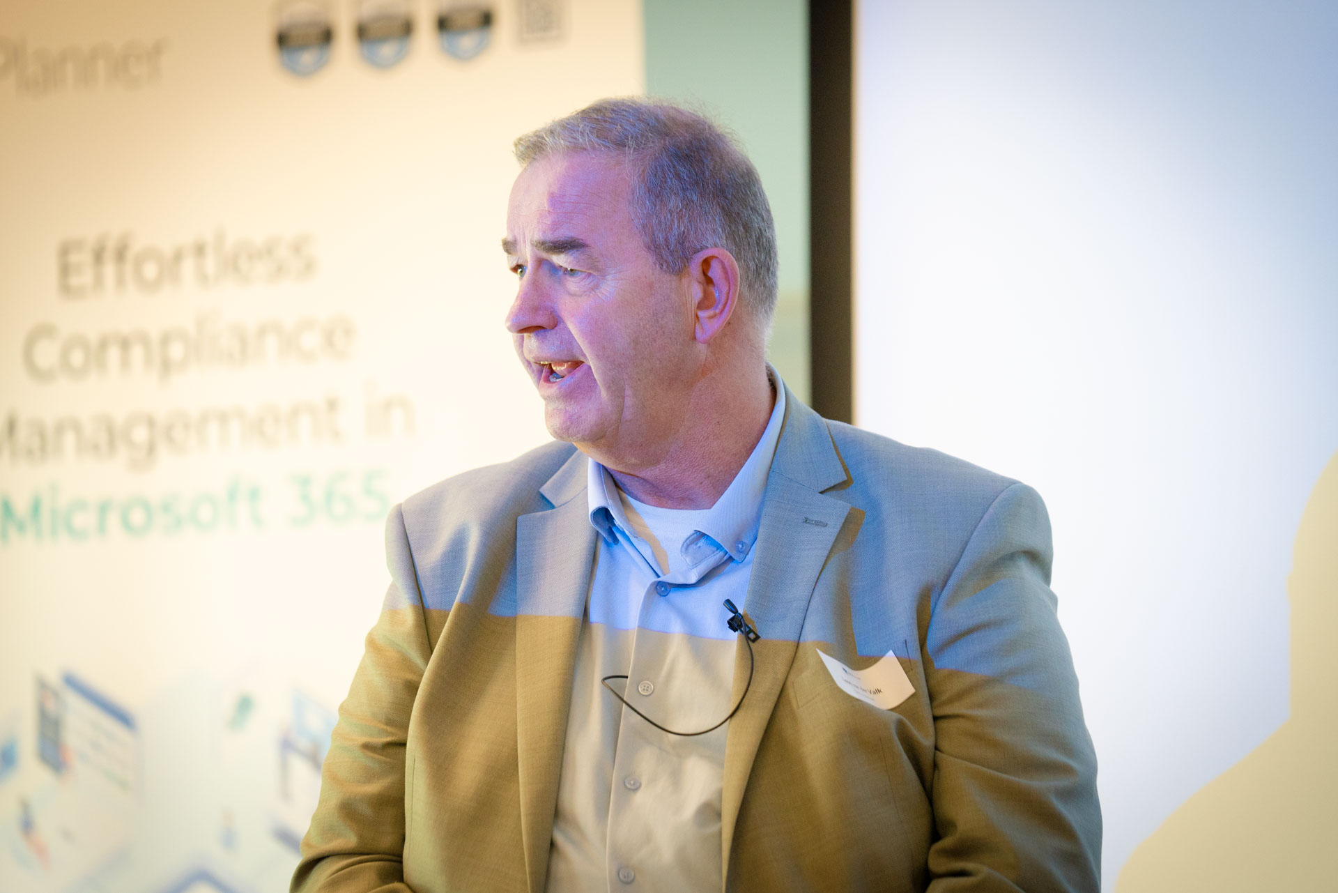 Close-up of a man speaking at a podium beside a screen reading Effortless Compliance Management in Microsoft 365.