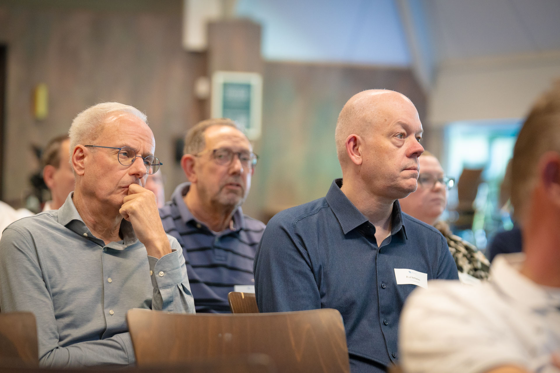Two seated men listen attentively during a talk, one resting his chin thoughtfully on his hand.