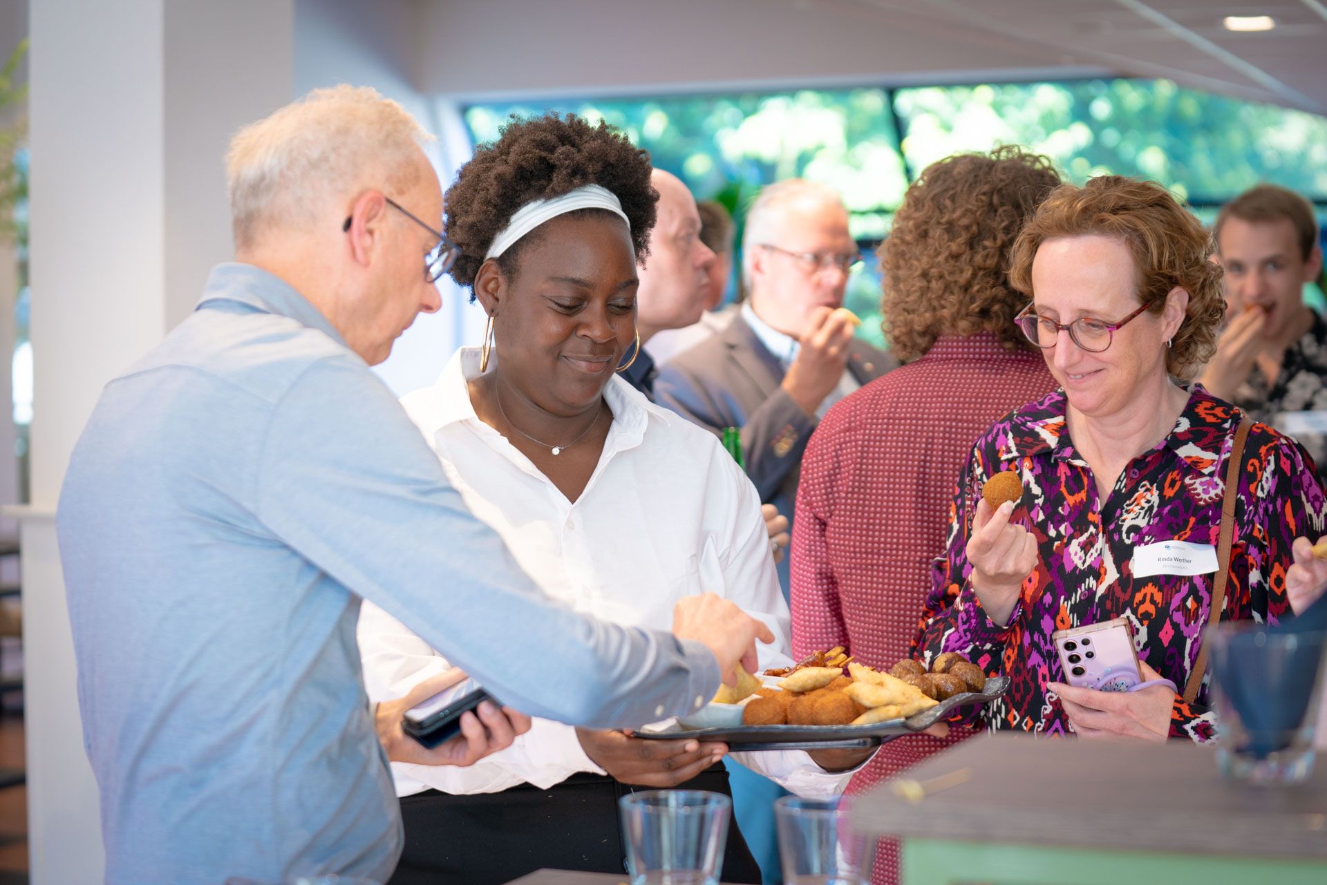 Three guests gather around a tray of fried snacks, with one of them reaching to take a bite.