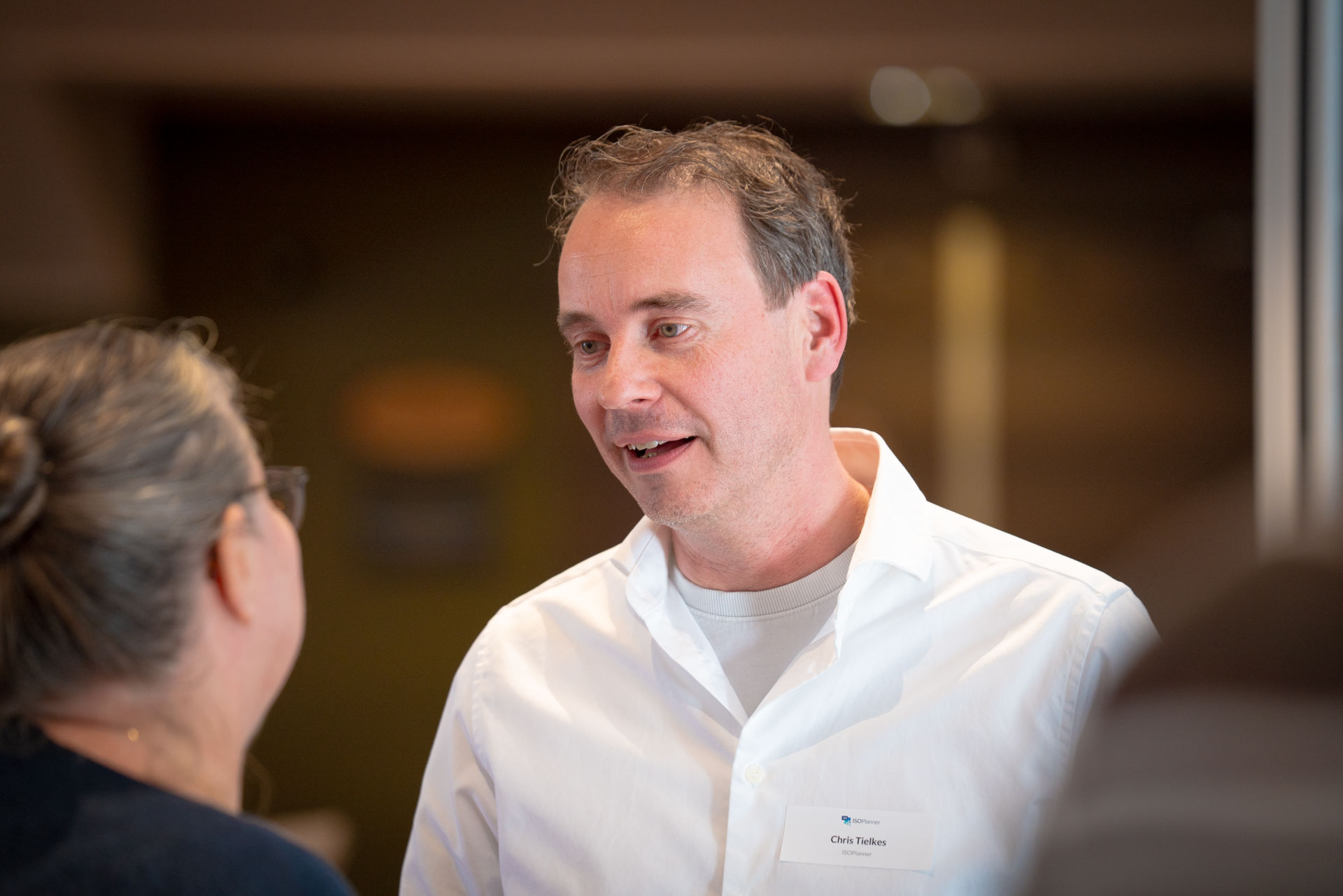 A man talks animatedly during a conversation at the reception, with a name badge visible on his shirt.