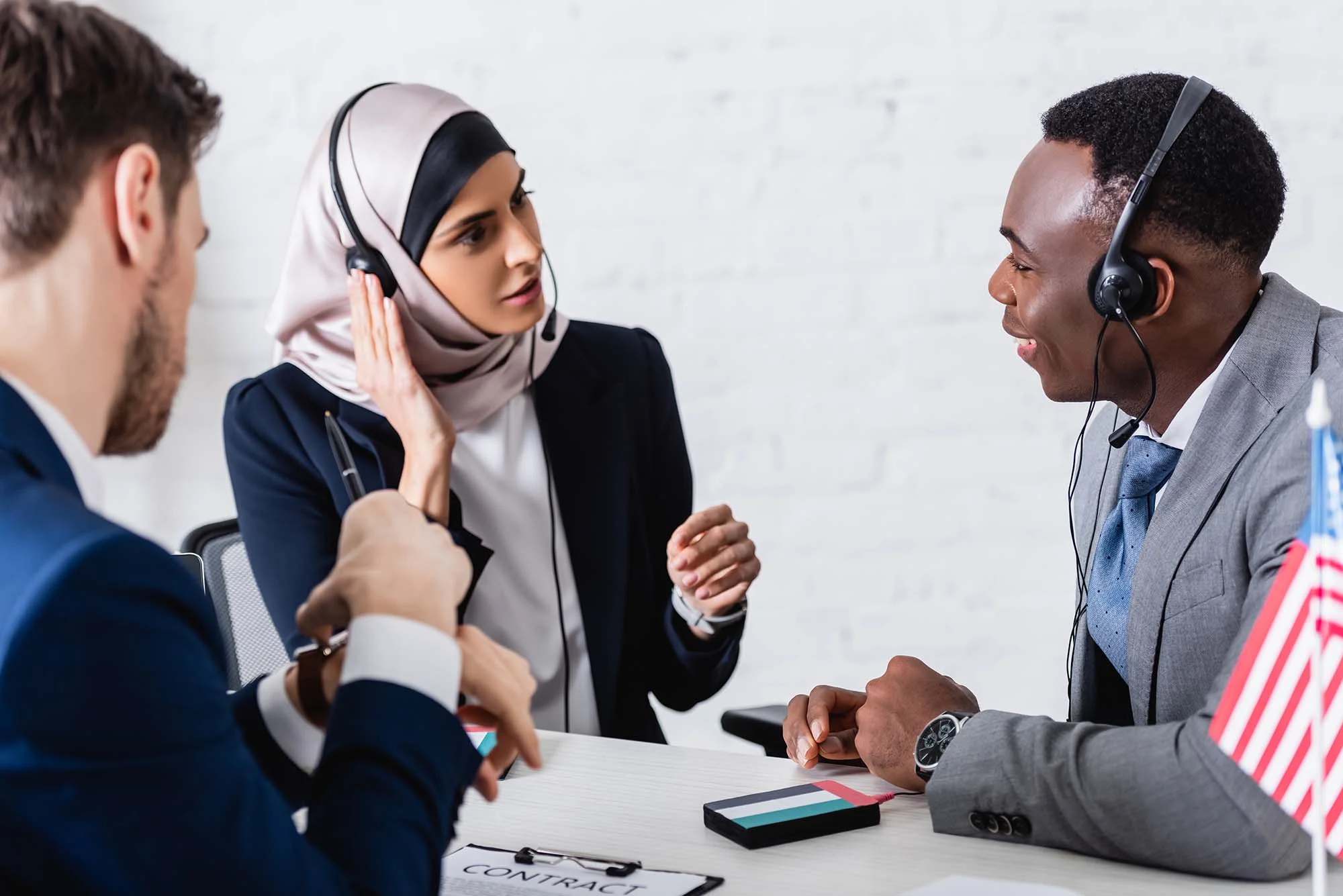 Three customer service representatives in business attire and headsets having a discussion at a desk with a contract and American flag.