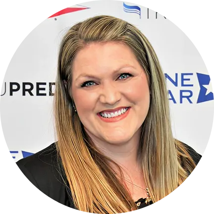 Smiling woman with long blonde hair wearing a black top in front of a backdrop with partial text and star logo.