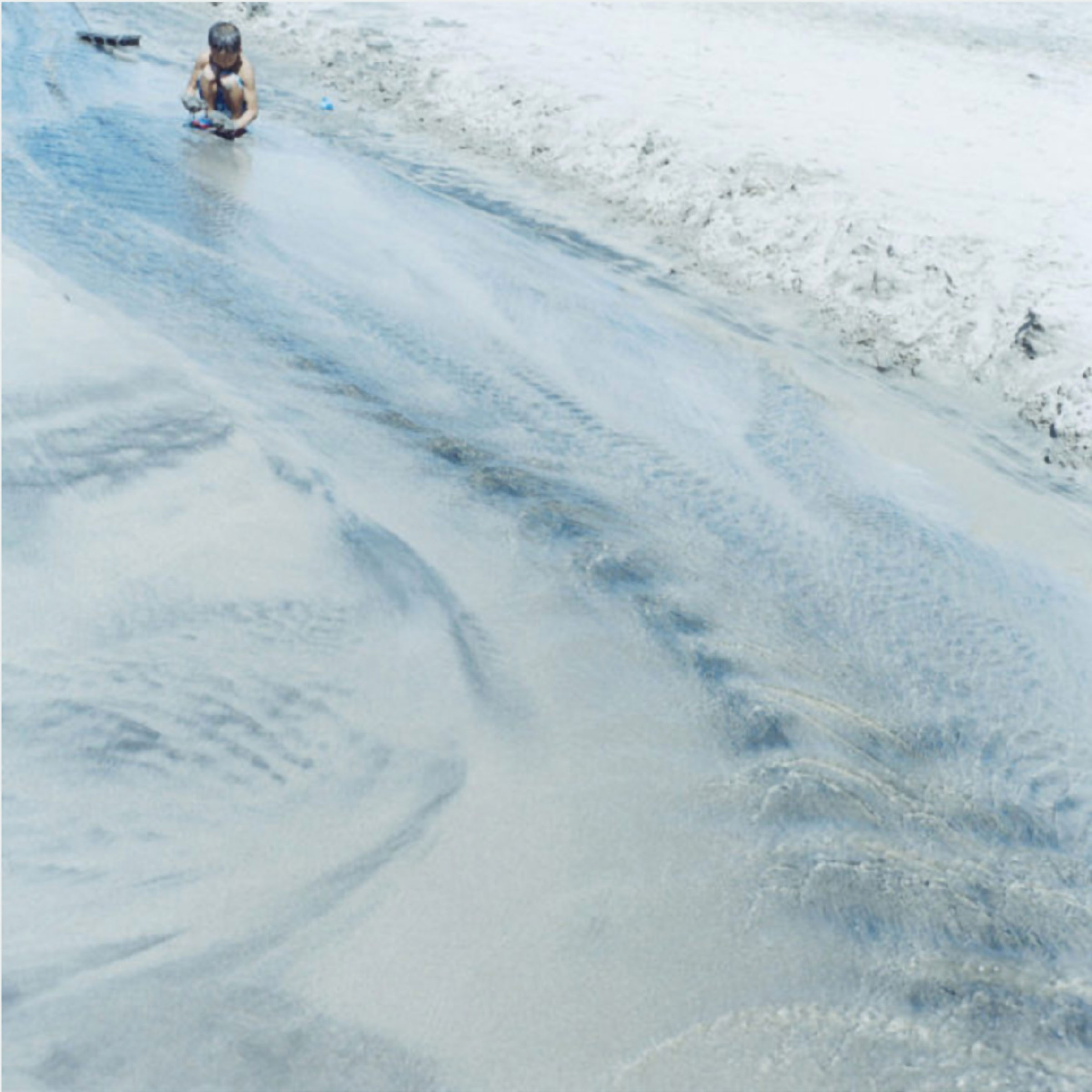 Rinko Kawauchi reference image: a child crouches at the water’s edge while shallow waves create abstract patterns