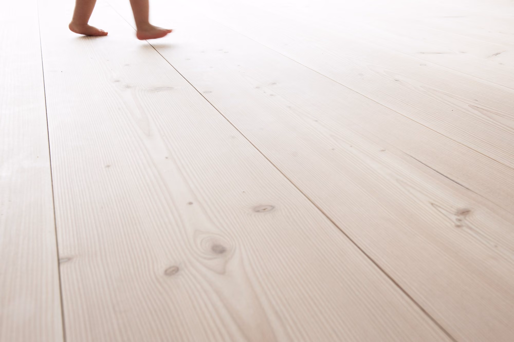 Barn går barfodet på et lyst plankegulv i nåletræ