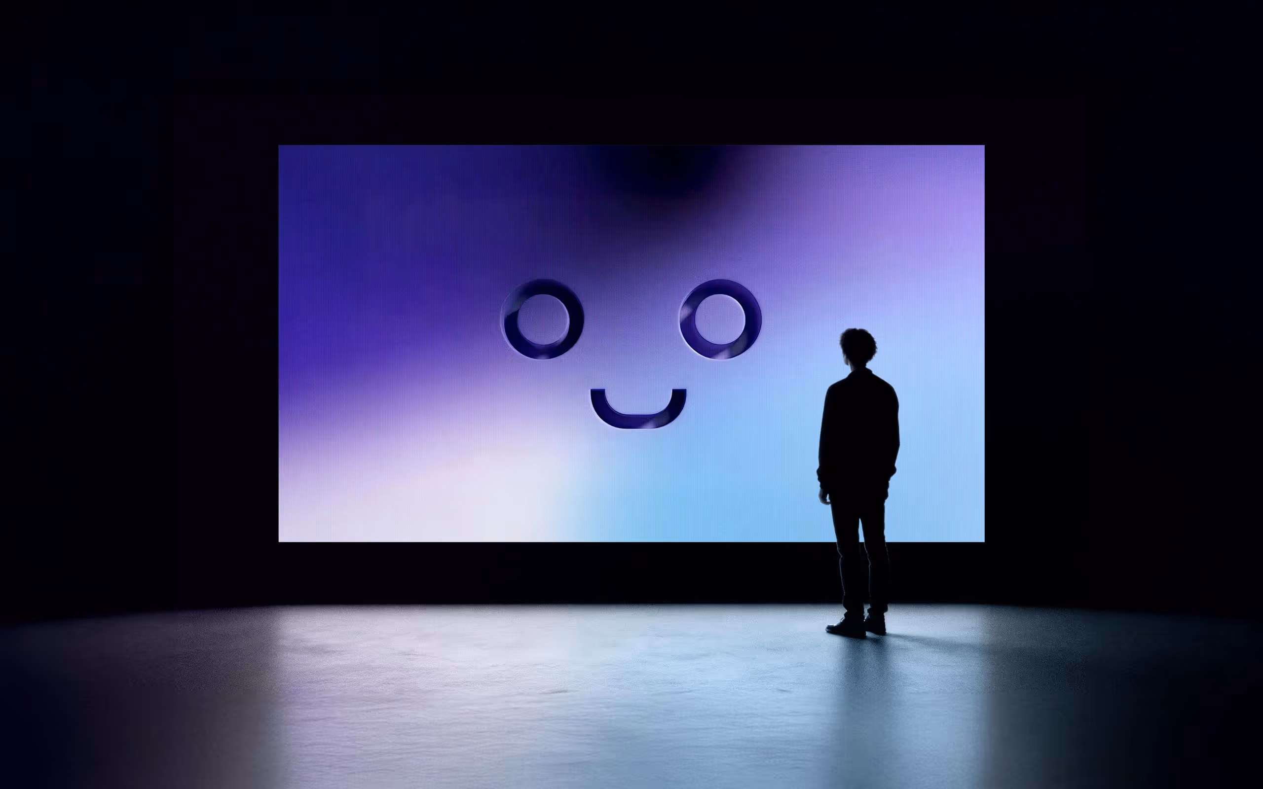 Silhouette of a person standing in front of a large screen displaying a simple smiling face with two round eyes and a curved mouth on a blue-purple gradient background.