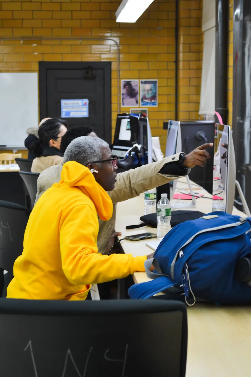 Student in yellow hoodie pointing at computer monitor during class