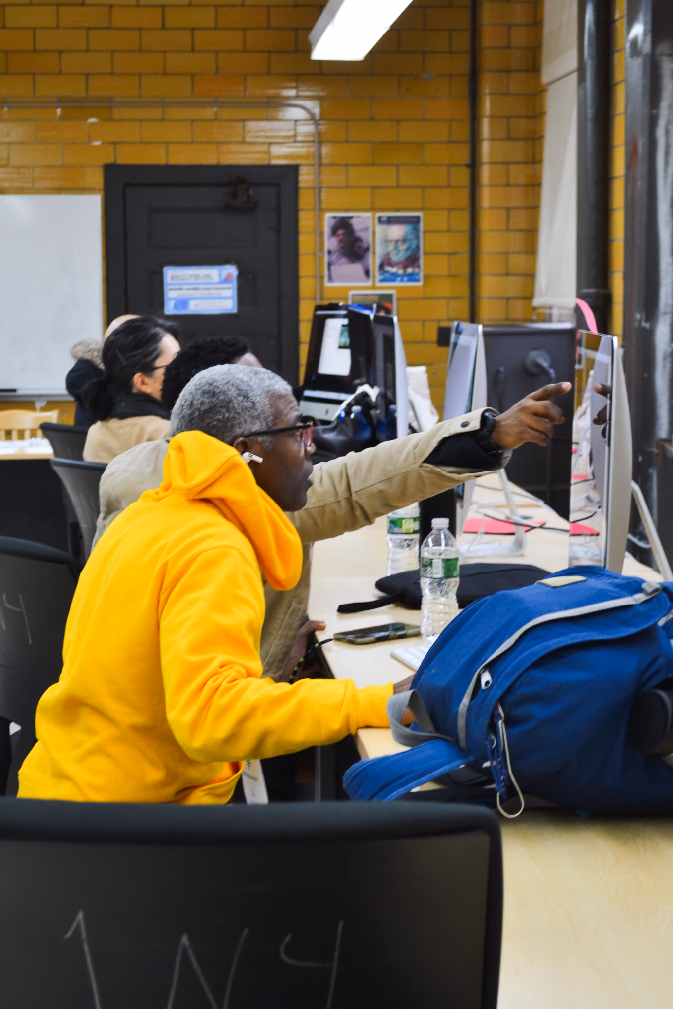 Student in yellow hoodie pointing at computer monitor during class