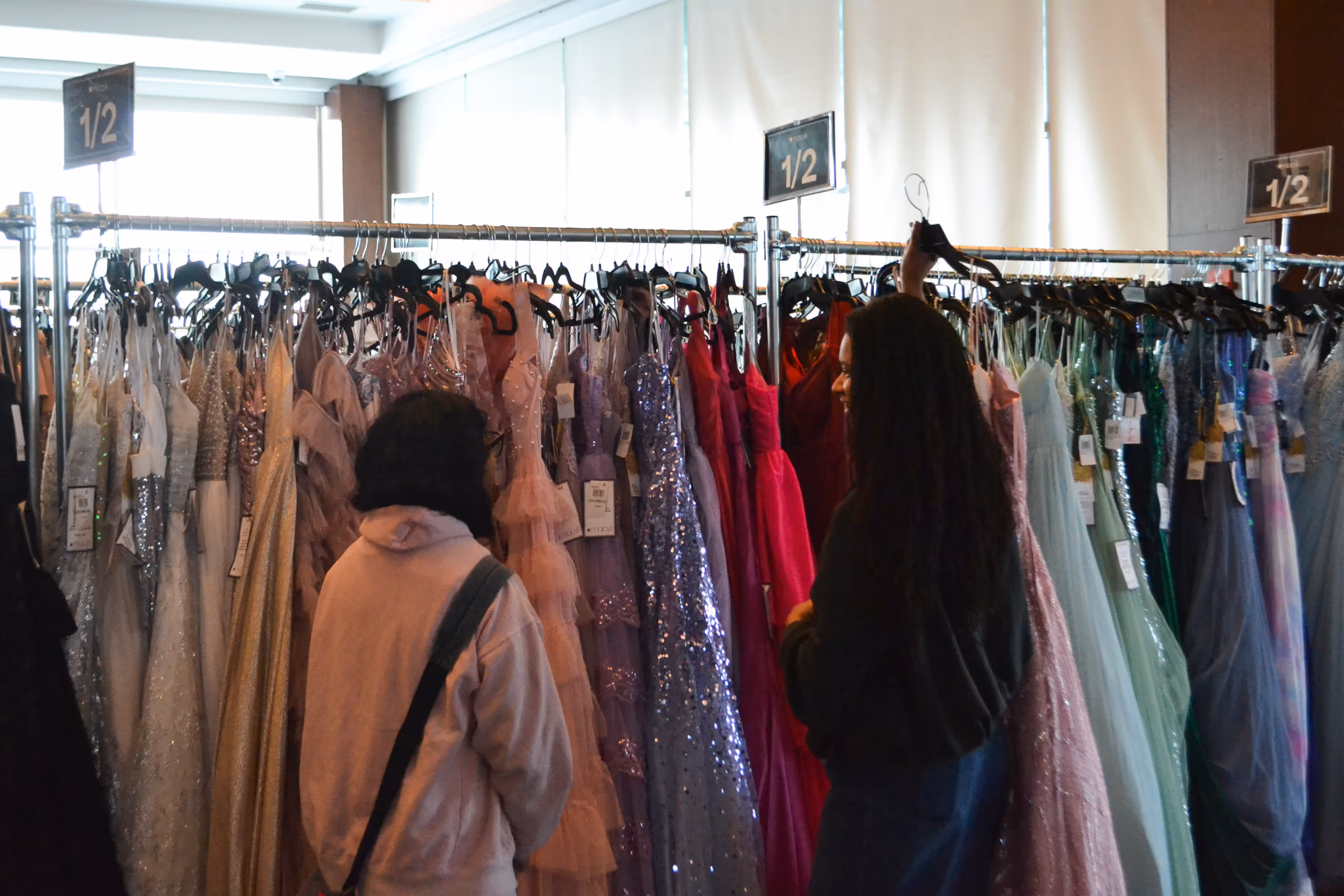 Students browsing colorful formal gowns on racks at a dress sale