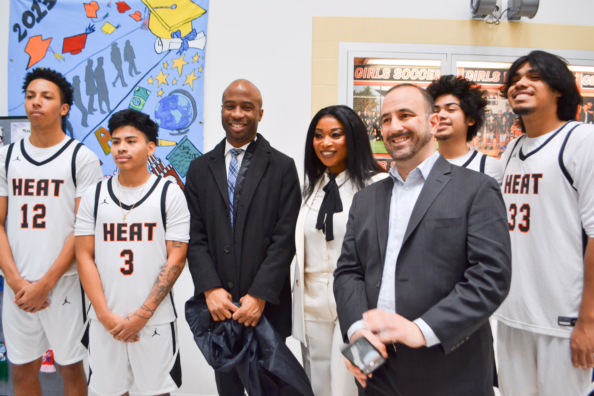 School administrators and Heat basketball players pose together indoors