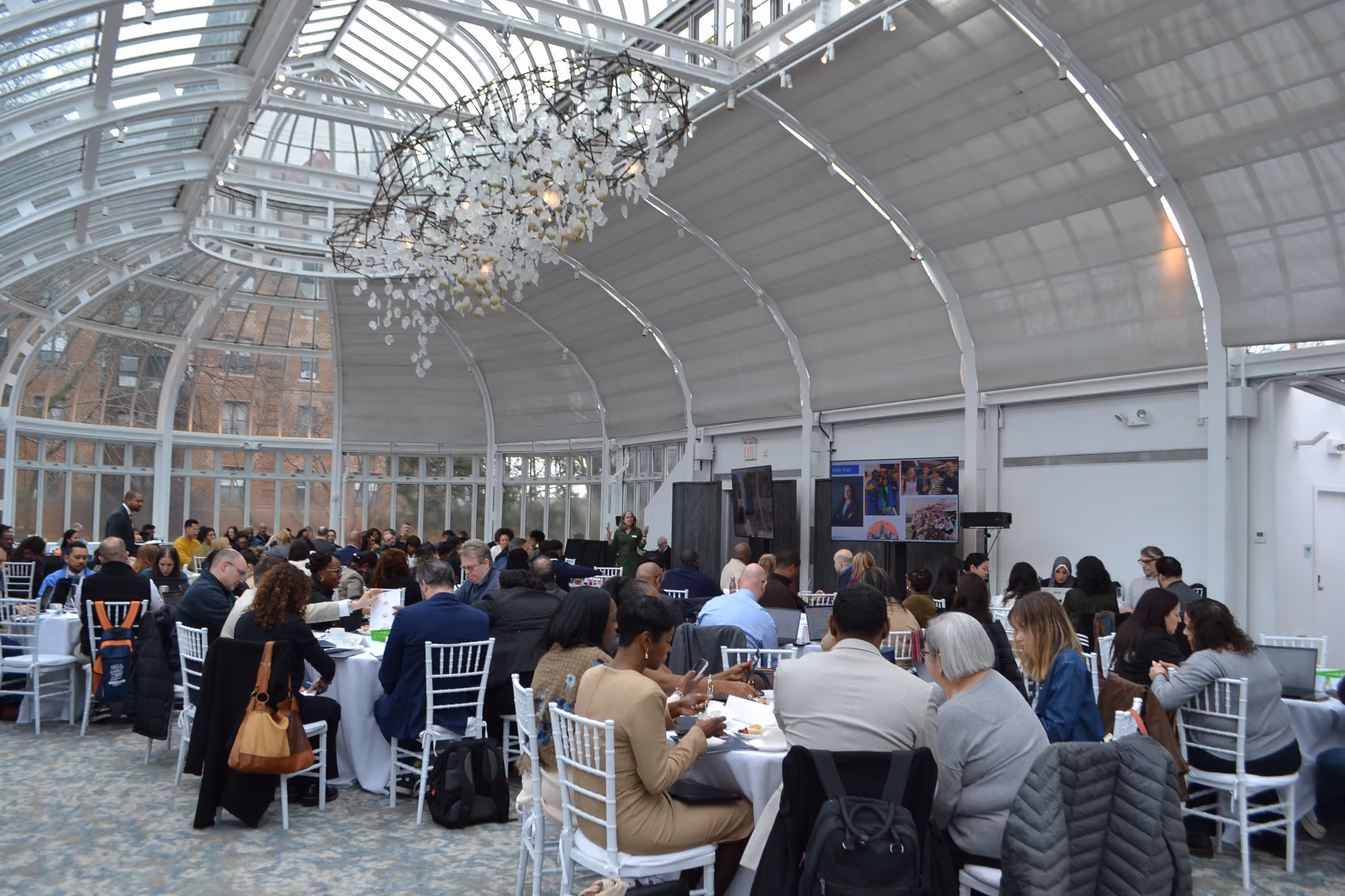 Attendees seated at round tables during a school district event in a glass pavilion