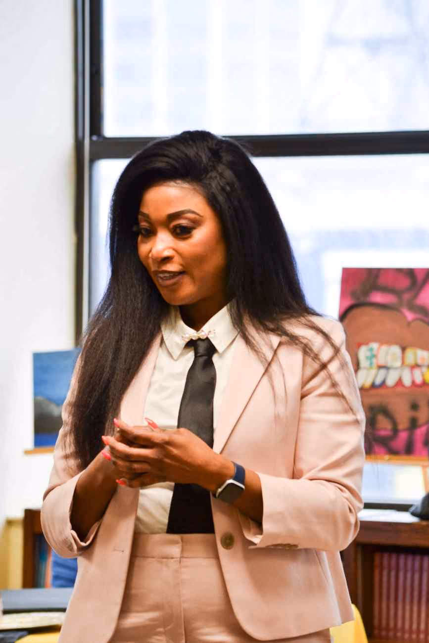 Woman in blazer and tie speaking to a classroom audience