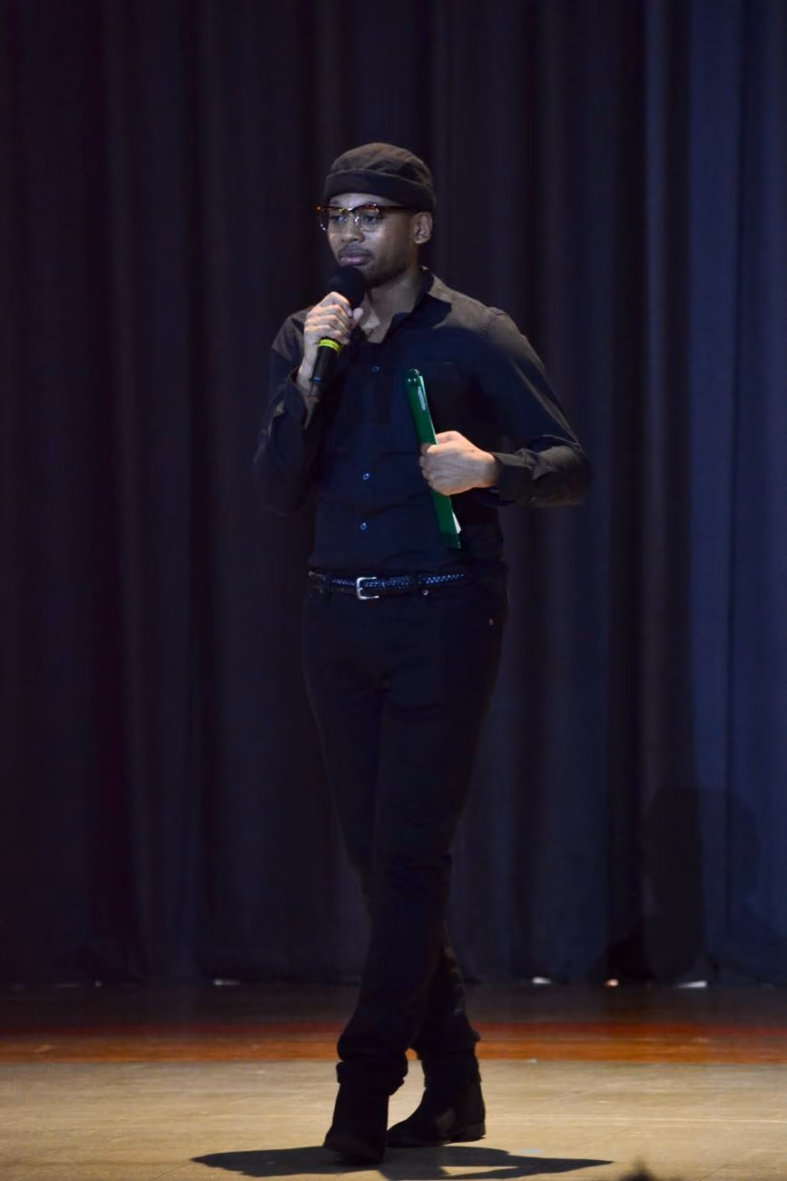 Student speaking into microphone on stage holding green folder