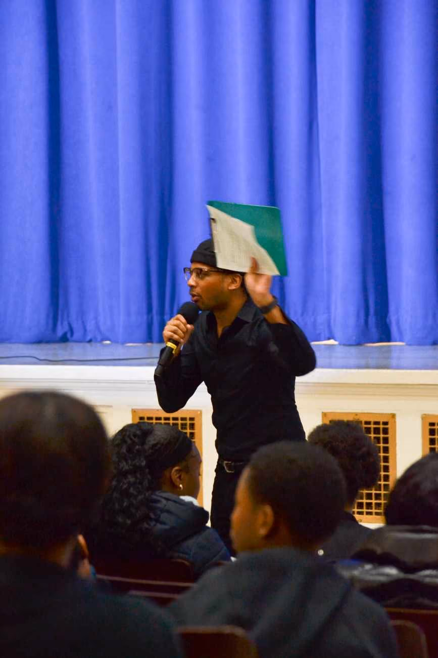 Speaker addresses student audience holding microphone and folder