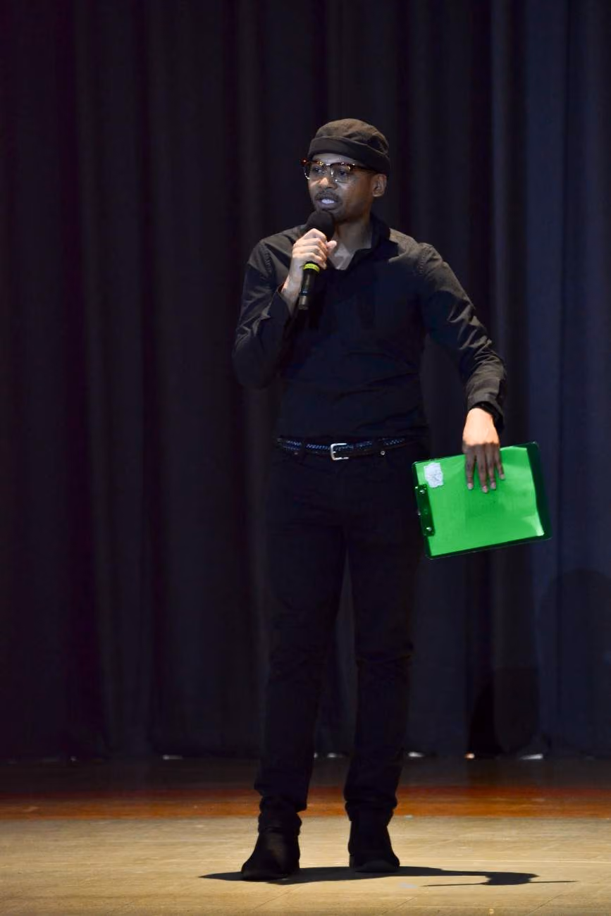 Student emcee speaking on stage holding microphone and clipboard