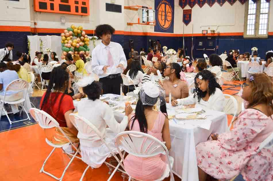 Students dressed up gathered at decorated tables during school tea party event