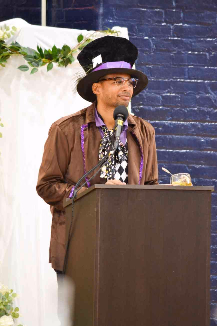 Person in Mad Hatter costume speaking at a podium with microphone