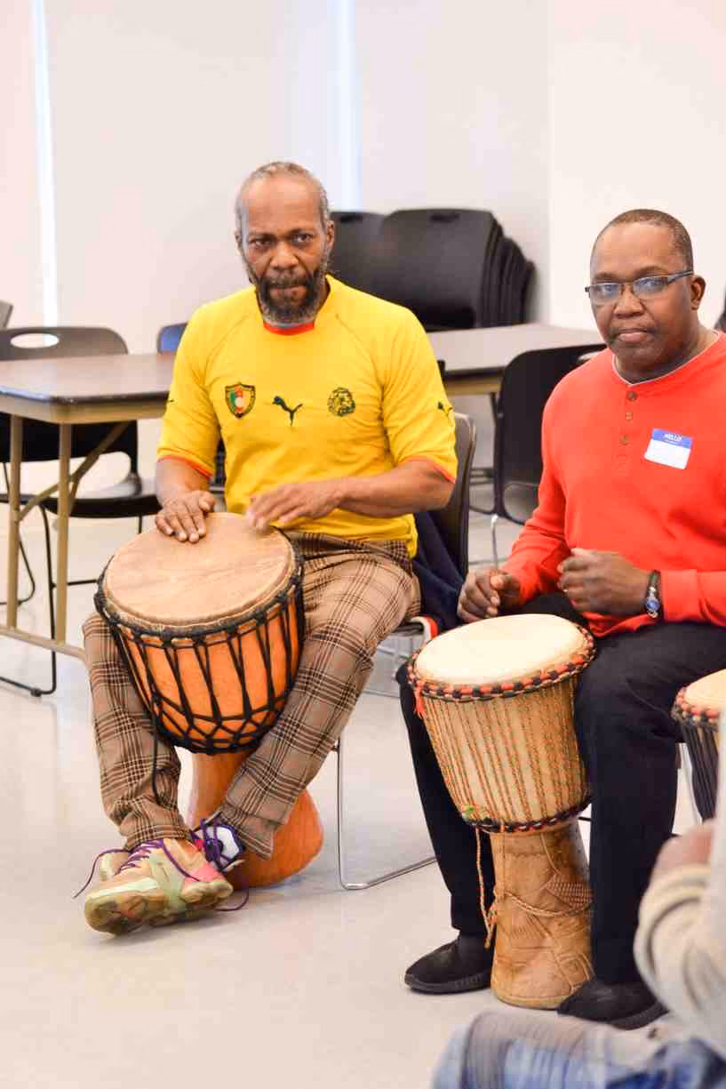 Two men playing djembe drums during a school arts workshop