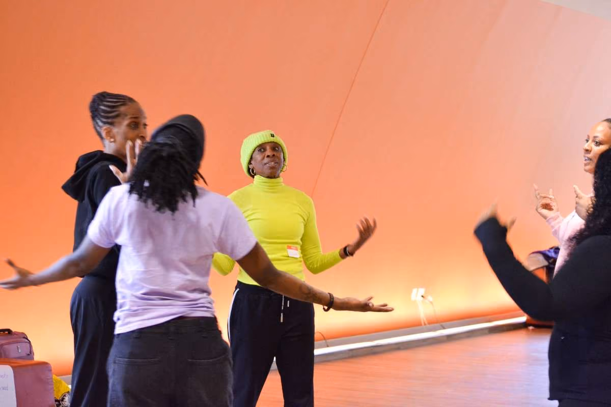 Instructor in yellow leads a movement activity with students in a dance studio