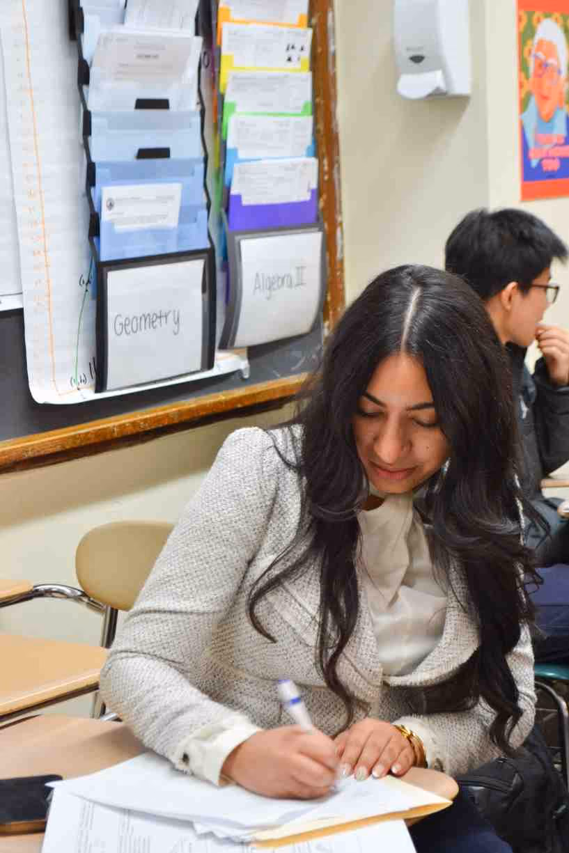 Student writing at desk in high school math classroom