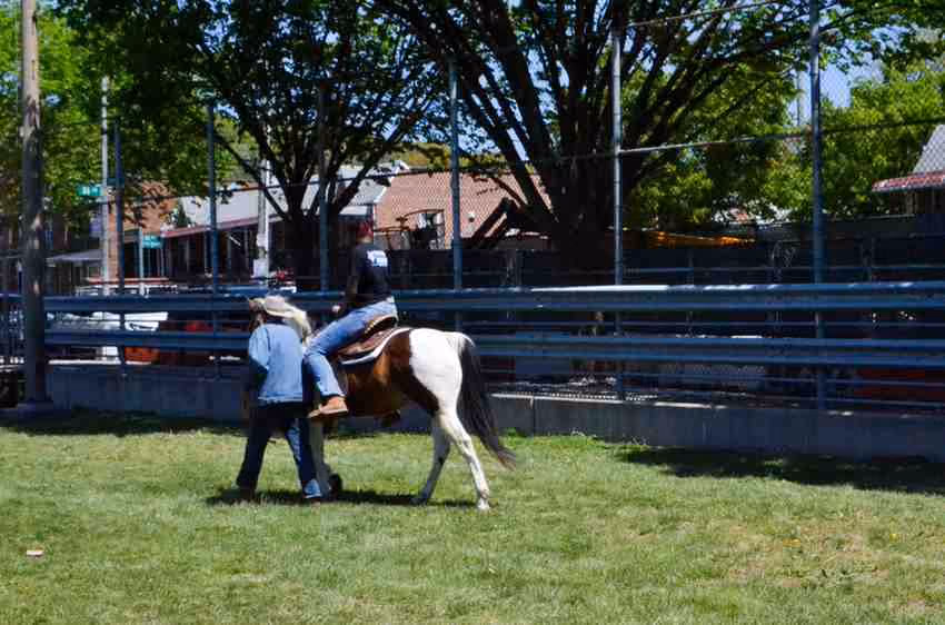 Student riding a pony assisted by an adult at outdoor event