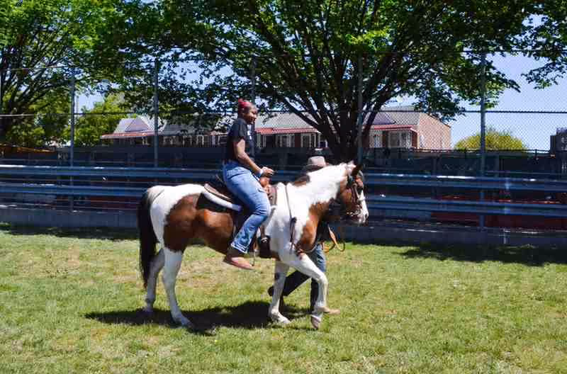 Student riding a paint horse led by instructor at outdoor event