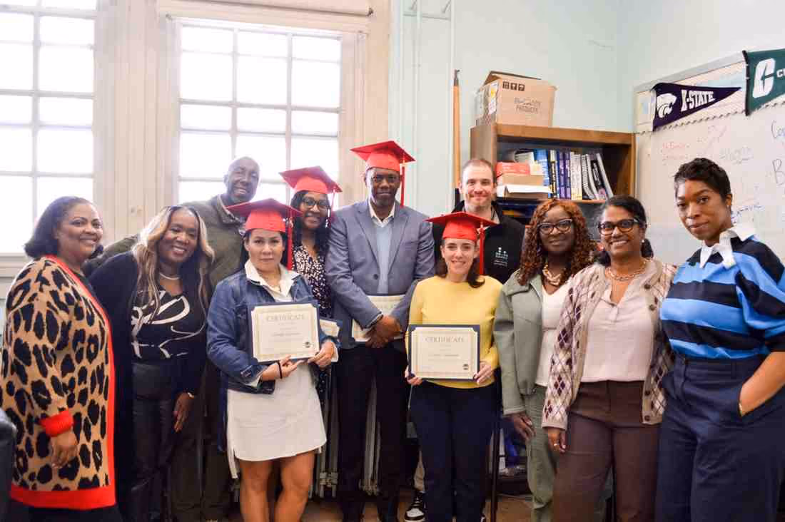 Students and staff celebrating certificate graduates in red caps indoors