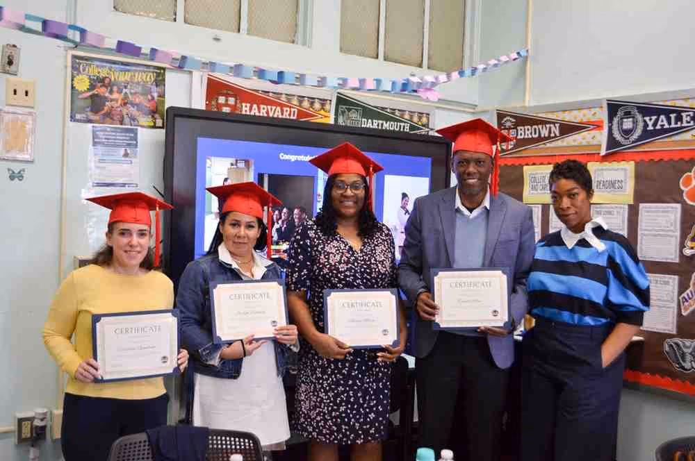 Five graduates holding certificates in a school college readiness classroom