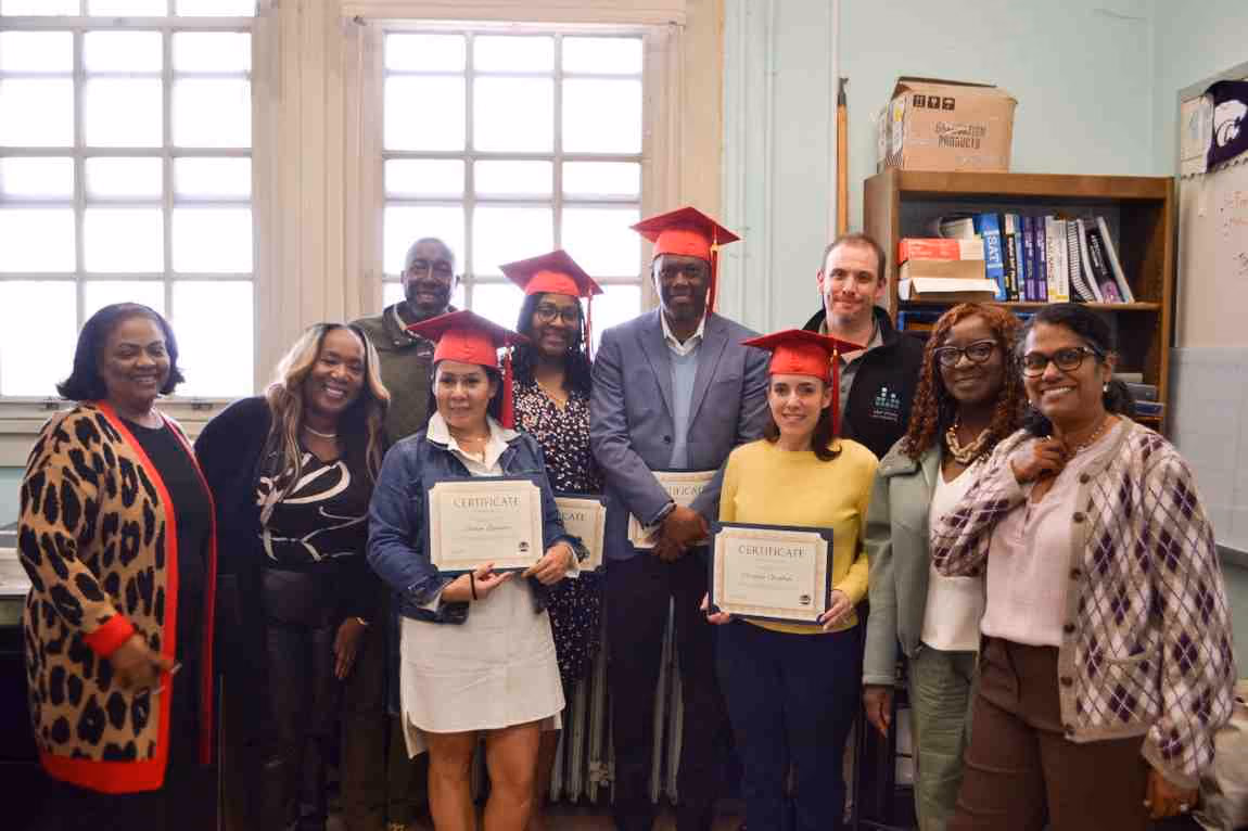 Graduates in red caps holding certificates pose with staff indoors