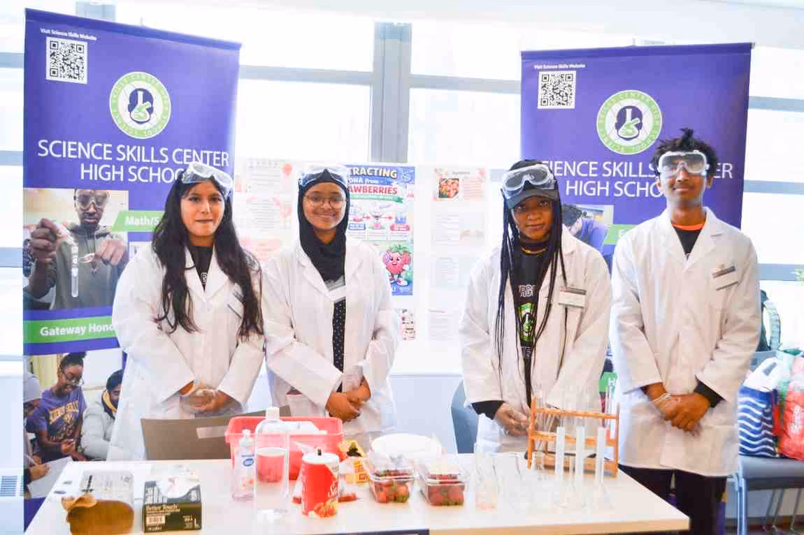 Four Science Skills Center High School students in lab coats at science fair booth