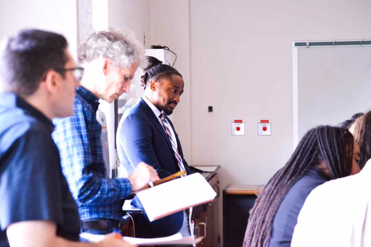Educator in suit and tie discussing notes with colleagues in classroom