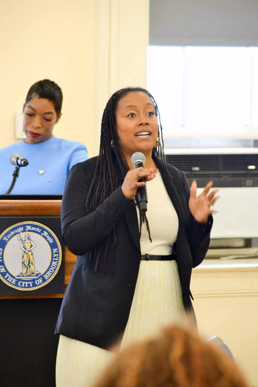 Woman speaking at microphone near City of Brooklyn podium
