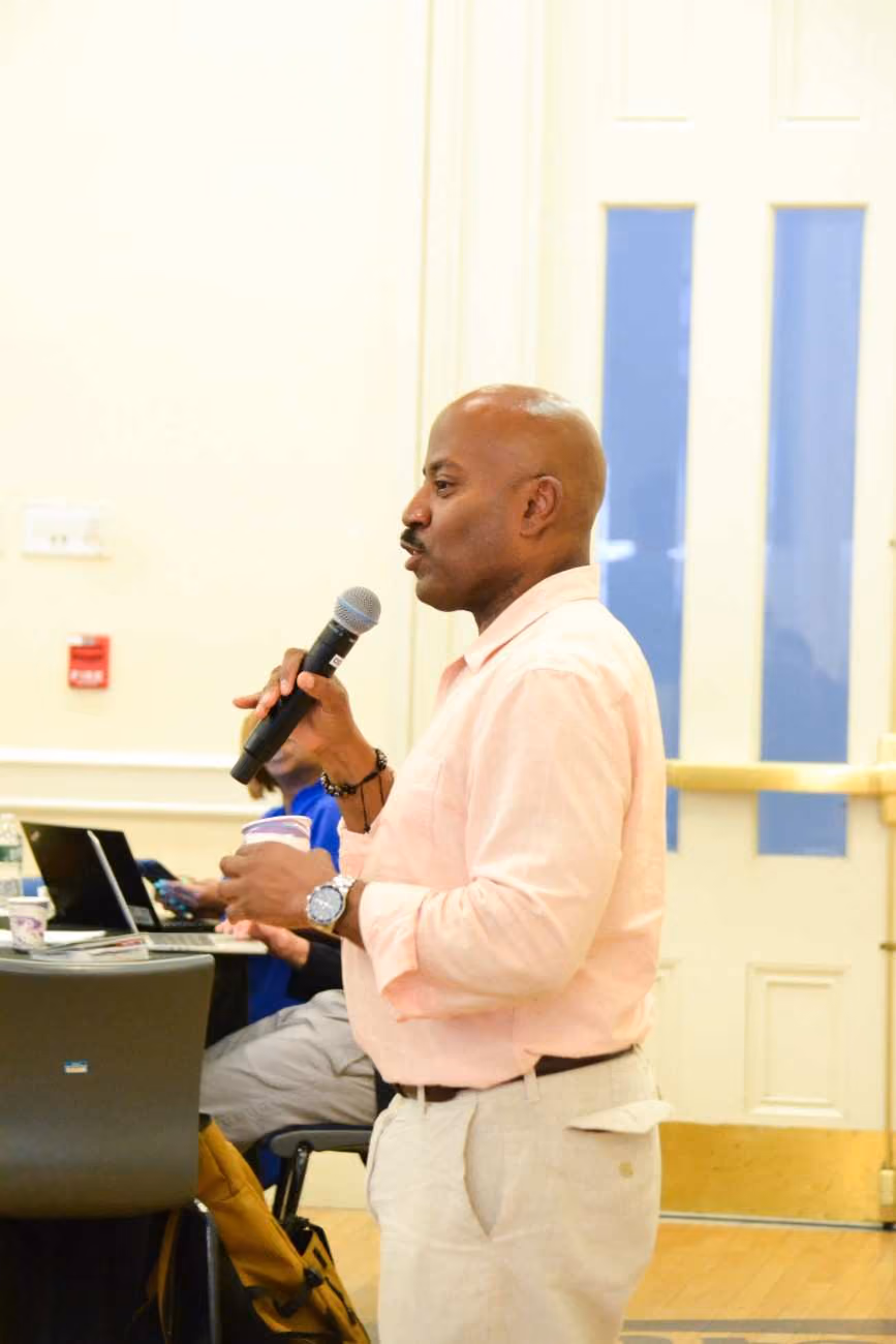 Man in pink shirt speaking into microphone at school event