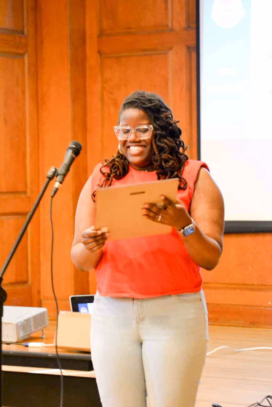 Woman smiling at podium holding folder during school presentation