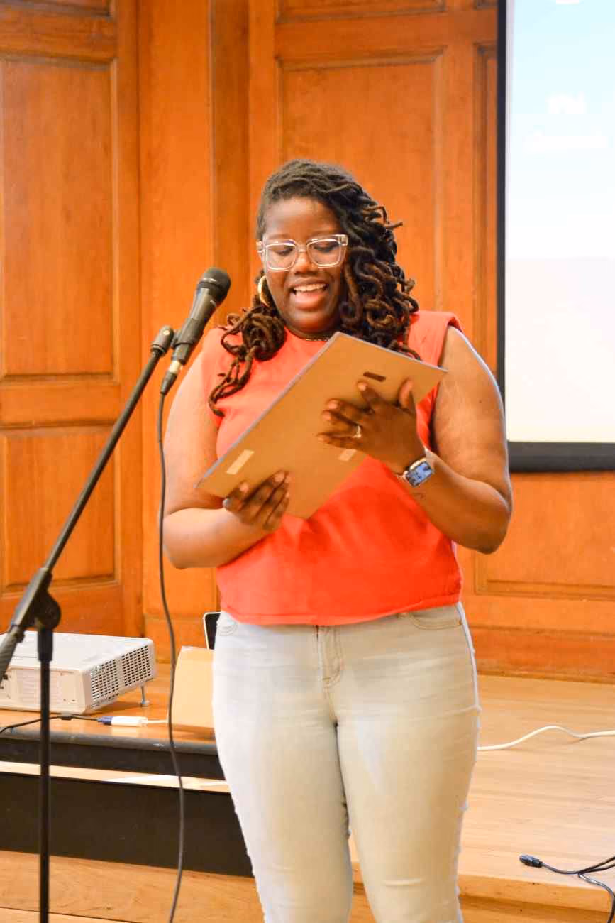 Woman speaking at microphone reading from folder on stage