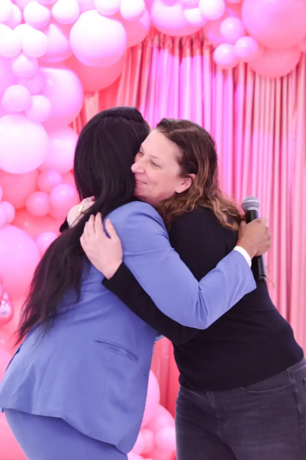 Two women embracing at a school event with pink balloon backdrop