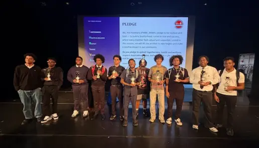 Students holding trophies on stage in front of a pledge screen