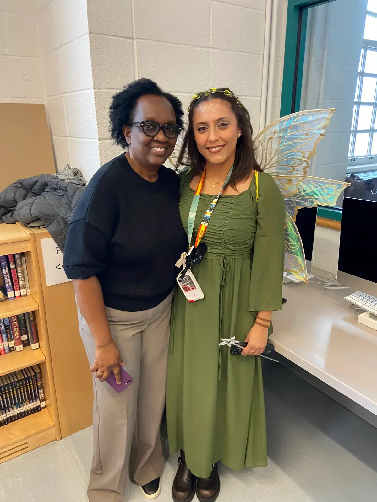 Two staff members pose together one wearing a fairy costume in school library