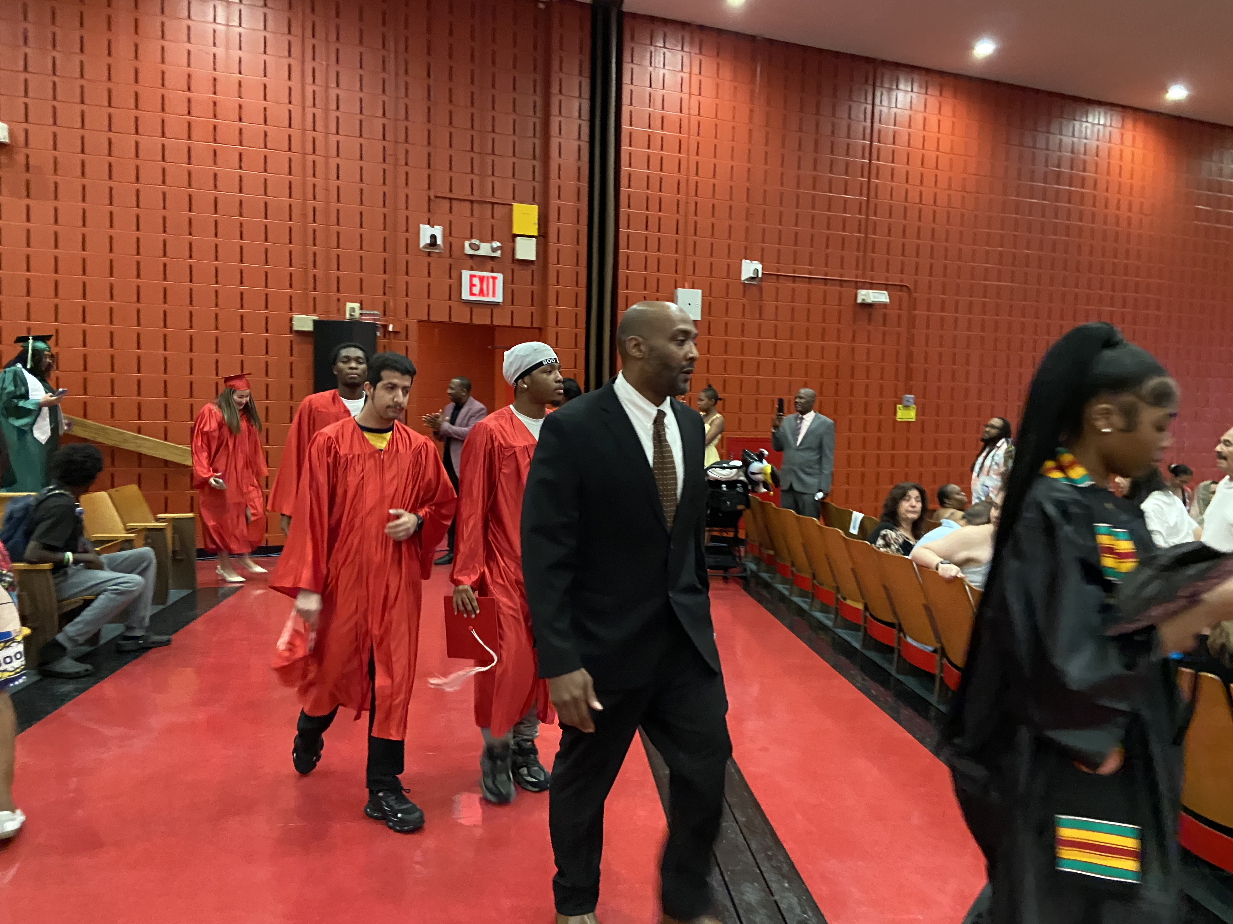 Students in red graduation gowns processing through auditorium during ceremony