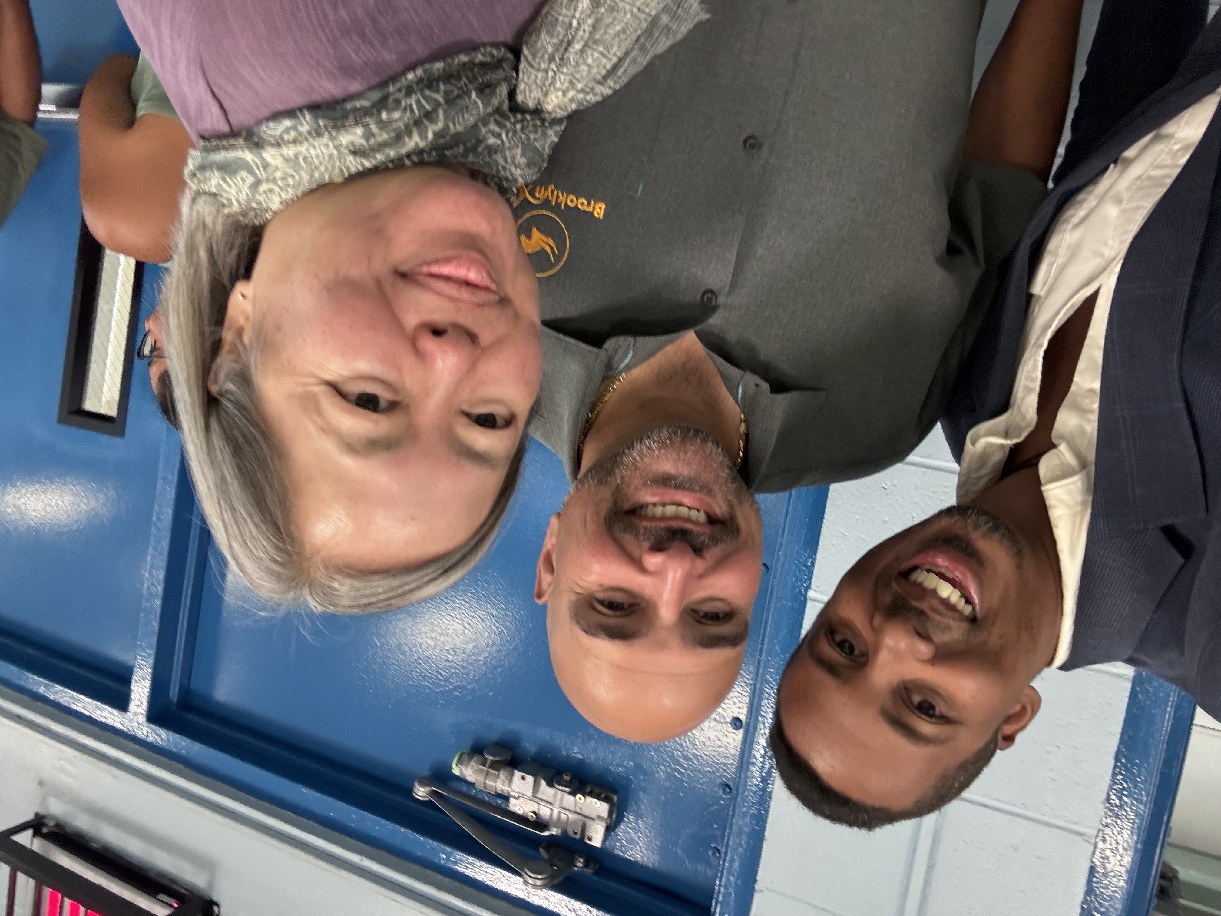 Three smiling adults posing together near a blue school door