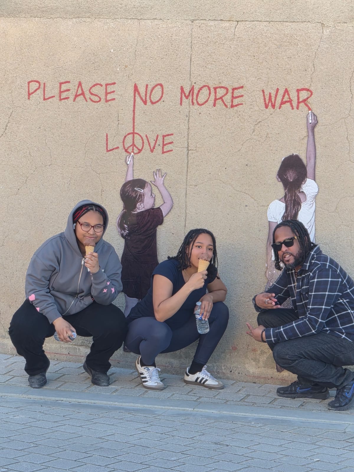 Three students posing with ice cream in front of Please No More War mural
