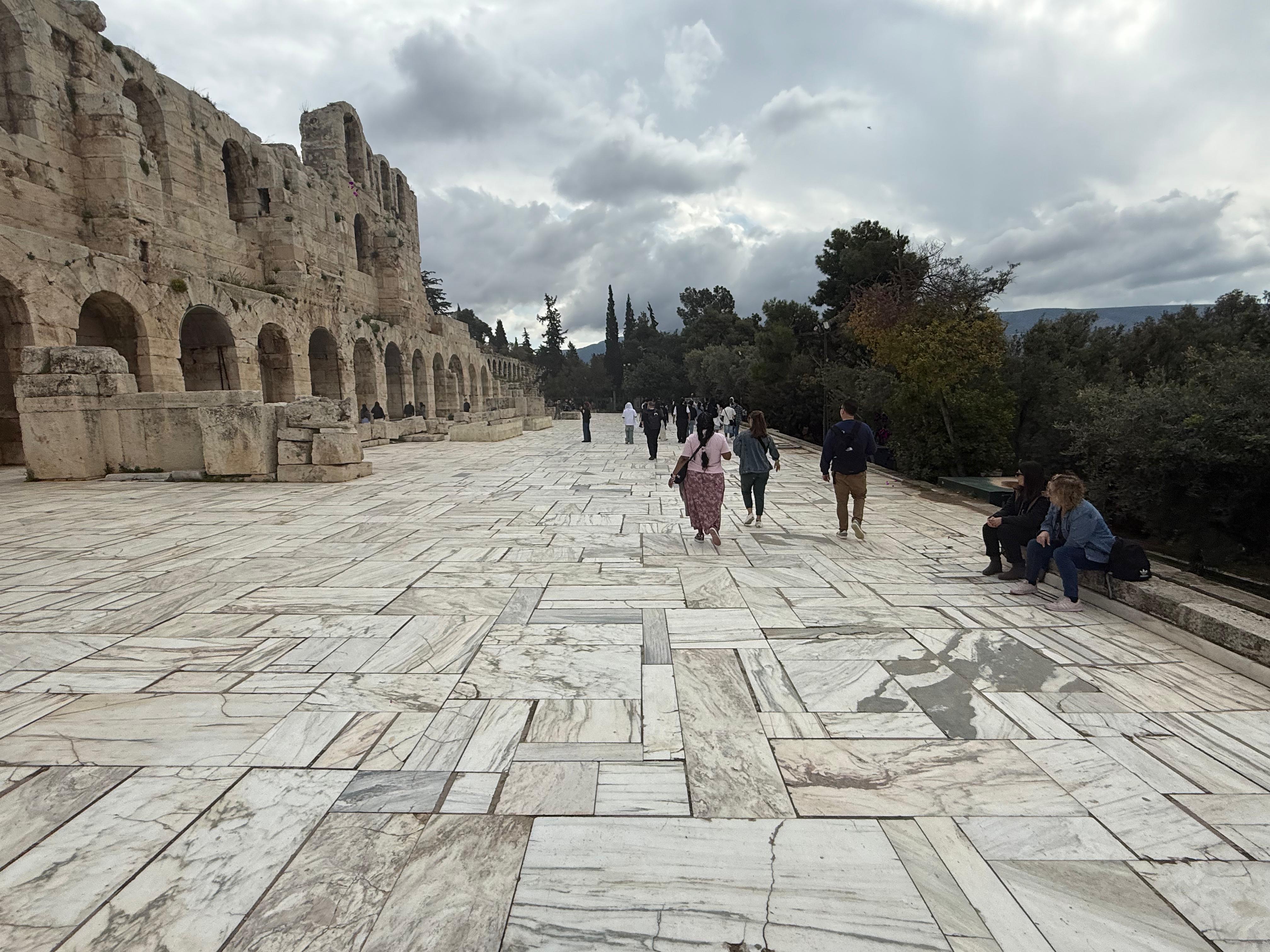 Students walking along marble promenade beside ancient Greek theater ruins