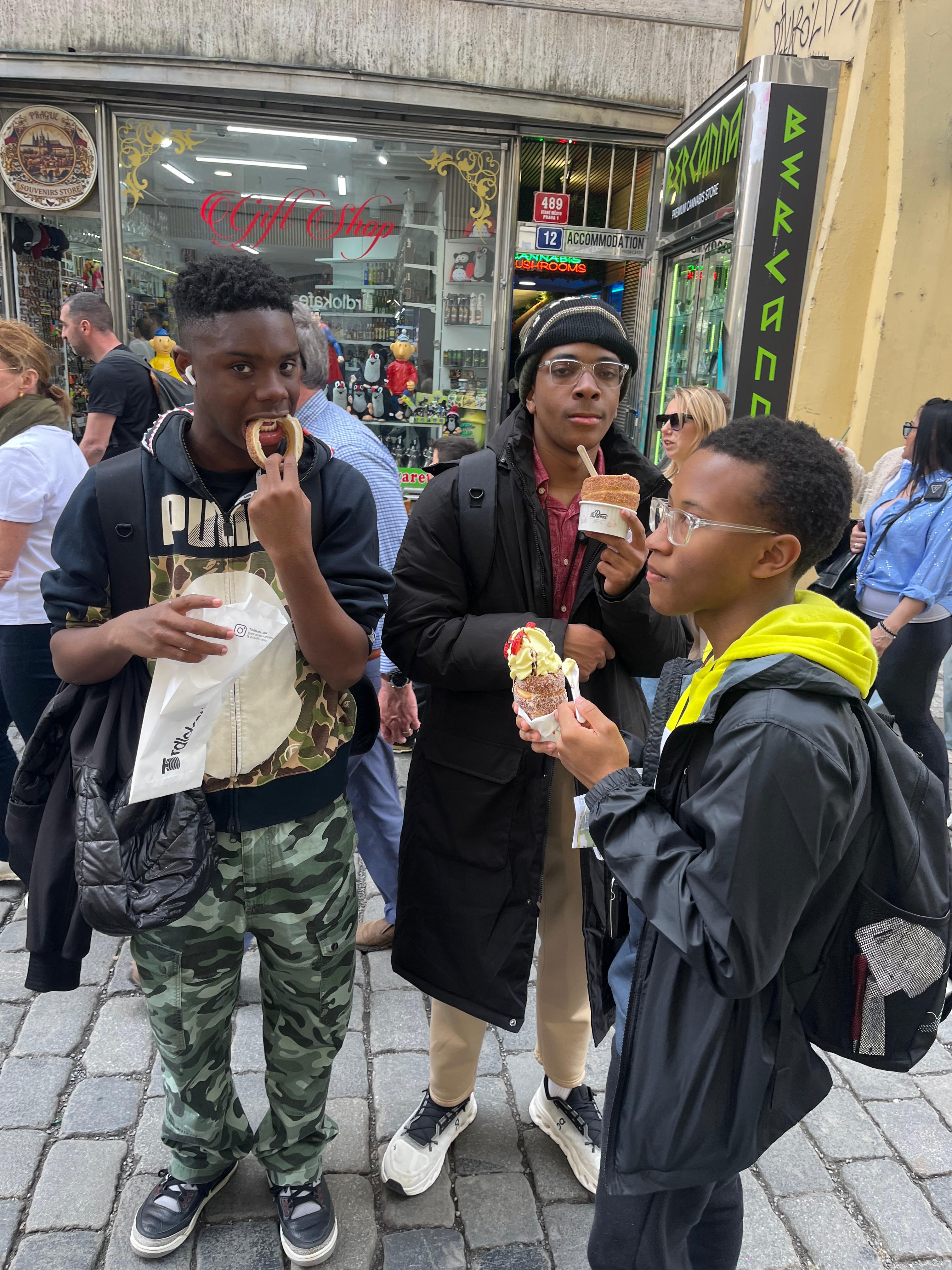 Three students eating street food on a cobblestone city street