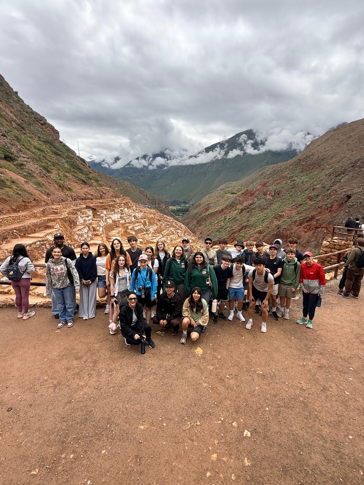 Students posing at Maras salt mines terraces in Peru mountains