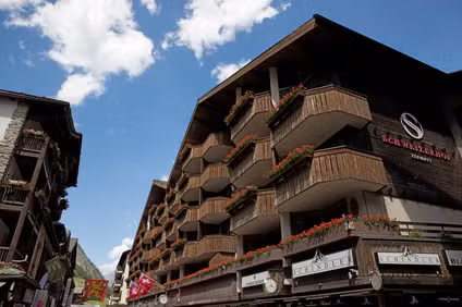 Hotel Schweizerhof in a Swiss alpine village with wooden balconies and Swiss flags under a blue sky.